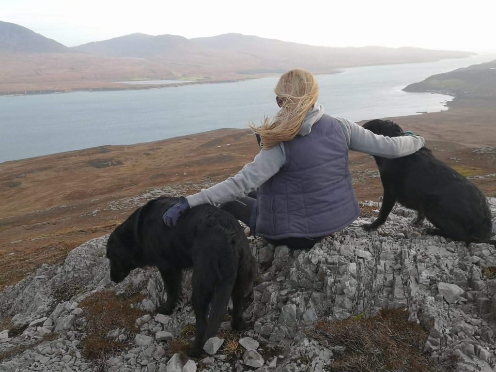 Woman and two dogs sat on hill top
