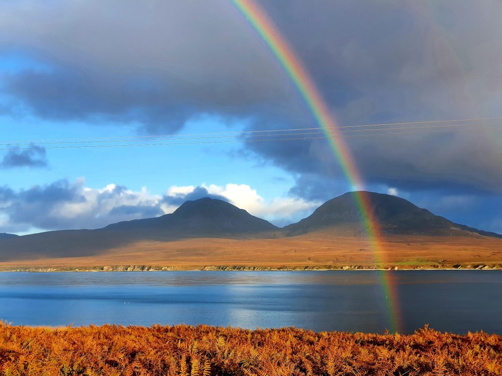 Rainbow over the sea with hills in the background.
