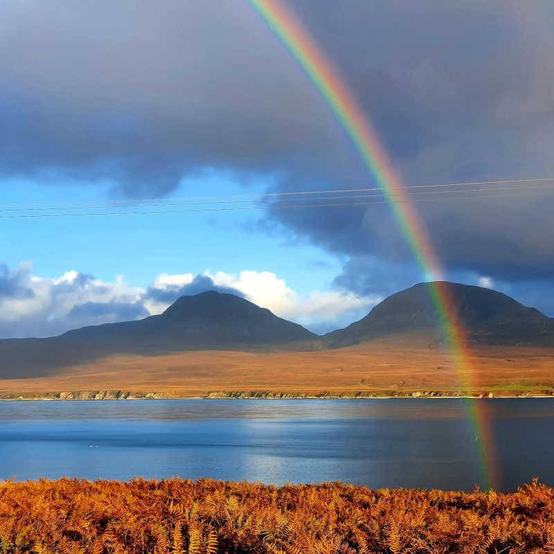Rainbow over the sea with hills in the background.
