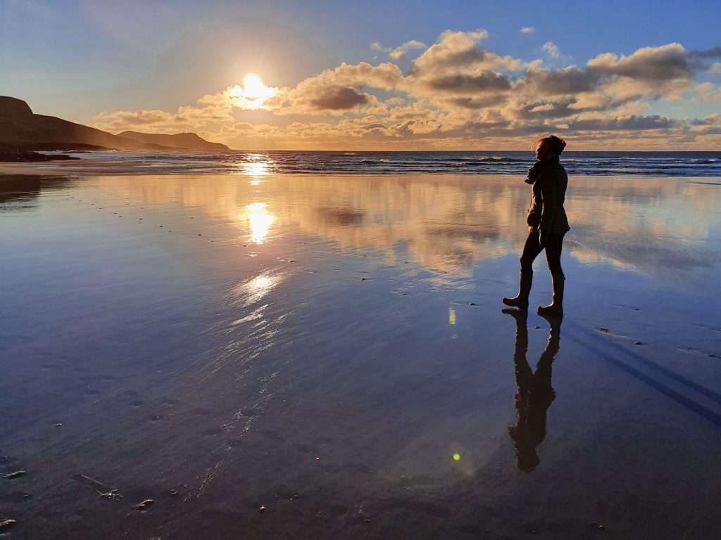 Lady walking on sandy beach at sunset