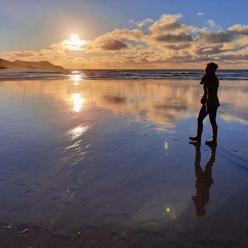 Lady walking on sandy beach at sunset