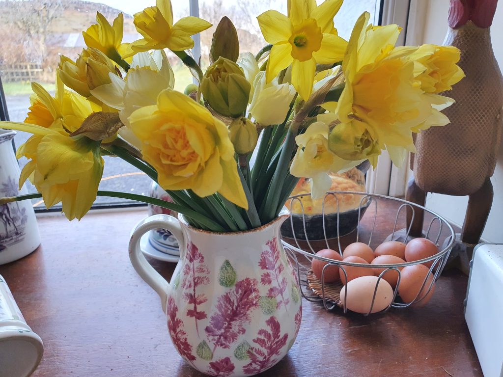 flowers in a jug, with a basket of eggs behind