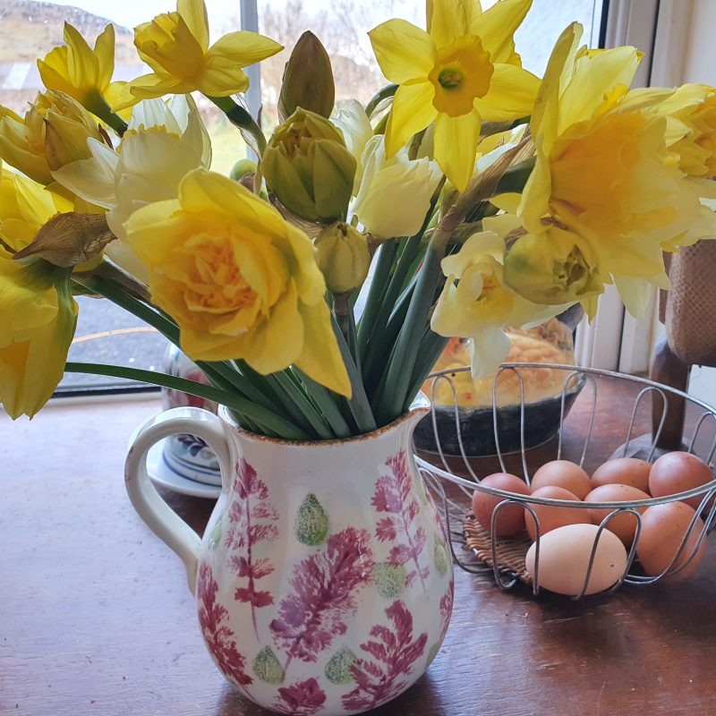 flowers in a jug, with a basket of eggs behind